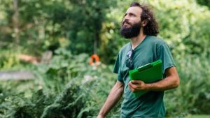 comment créer une entreprise de paysagiste - un homme habillé en vert parcourant un jardin paysager avec un bloc-notes